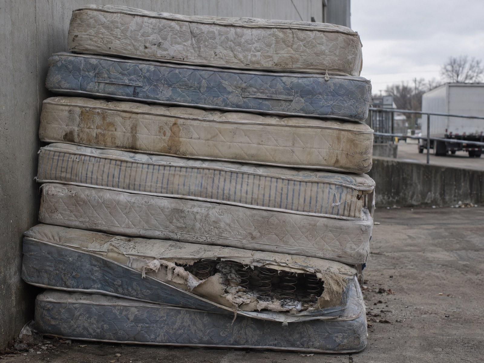 Illustrative stack of used mattresses against an industrial wall.
